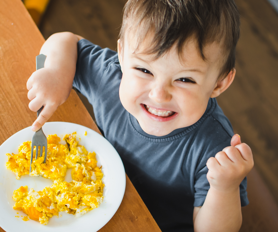 Photographie d'un enfant en train de manger un plat avec le sourire.
